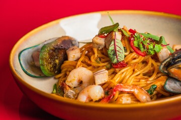 Closeup of pasta with shrimp and mussels on a toast on a red background