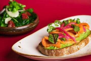 Closeup of salmon and avocado on a toast on a red background