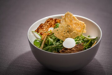 Closeup of a bowl of salad with greens, crackers and white truffle