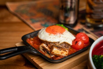 Closeup of Asian style fried egg on meat with tomato in a pan