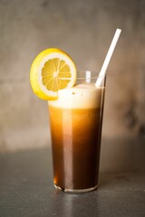 Vertical of a glass of iced cocktail with lemon and a straw