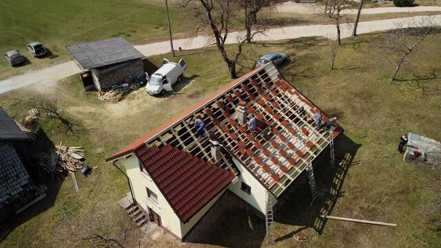 Crane shot descends on workers tiling roof on bare bones of new home