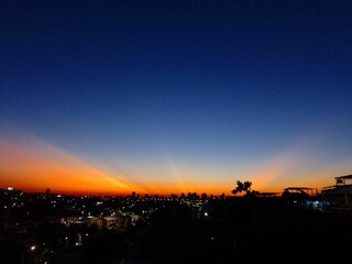 the sun rising behind some hills and trees with buildings in the background
