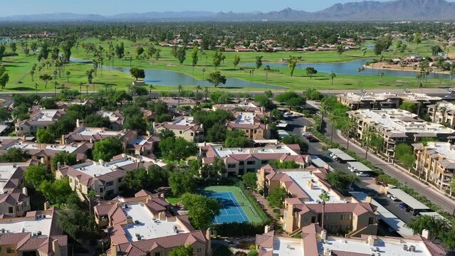 Southwest USA aerial view: lush golf courses, water features, and terracotta-roofed residences, with mountain backdrop and clear blue skies.
