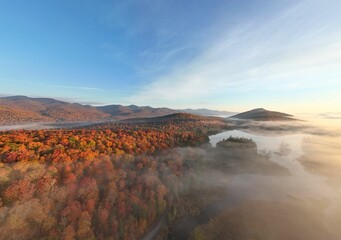 Scenic view of fall foliage on mountains with a river and forest in the foreground.