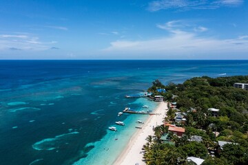 Aerial view of a coastal beach with crystal blue waters and white sand shoreline in Roatan Honduras