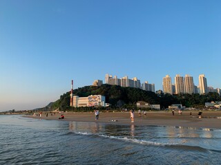 Obraz premium people walking on a beach near the ocean with skyscrapers in the distance: Busan, South Korea
