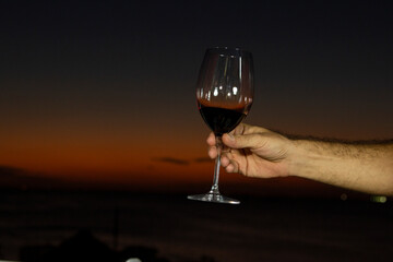 Copa de vino tinto, en la mano de una persona diciendo salud, con el atardecer de fondo