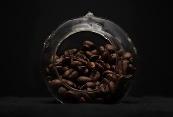 Jar filled with freshly roasted coffee beans sits atop a black background.