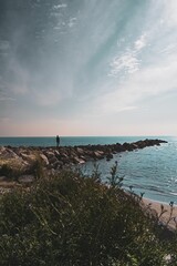 Woman walking on a  rock jetty surrounded by tranquil waters of the sea.