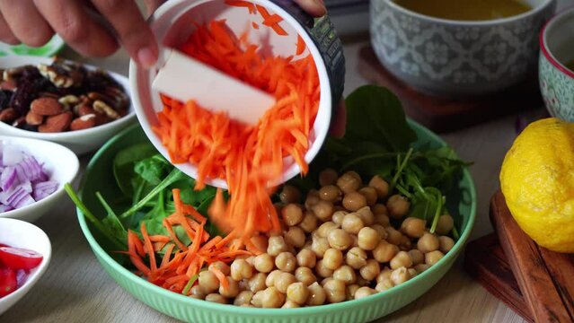 Handheld shot making of a salad adding carrots tomatoes spinach chick peas lemons onions nuts dressing in view