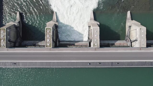 Aerial Shot of a Group of Cyclist on a Power Plant Dam With Open Gates with Water Flowing - Top Down