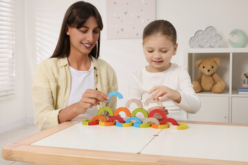 Motor skills development. Mother helping her daughter to play with colorful wooden arcs at white table in room