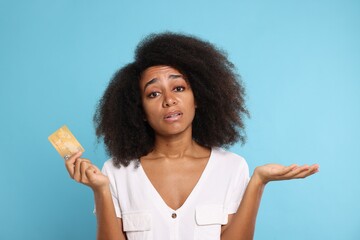Confused woman with credit card on light blue background. Debt problem