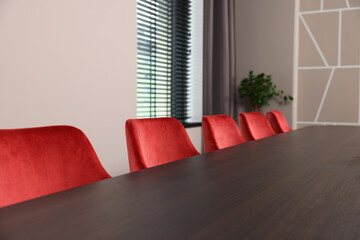 Stylish red office chairs and large wooden table in empty conference room