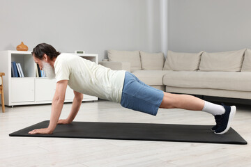 Senior man in sportswear doing exercises on fitness mat at home - obrazy, fototapety, plakaty