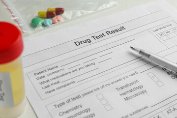 Drug test result form, pills and container with urine sample on light table, closeup