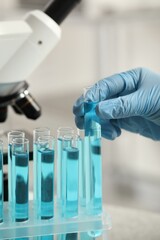 Fototapeta premium Scientist taking test tube with light blue liquid in laboratory, closeup