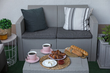 Outdoor breakfast with tea and croissants on rattan table on terrace