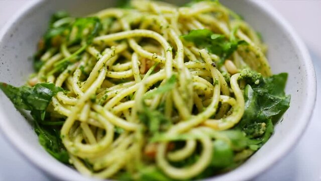 Spaghetti and pesto with rocket and pinenuts rotating in a bowl. HD footage of vegetarian italian pasta cooking. Plant-based and vegan recipe images.