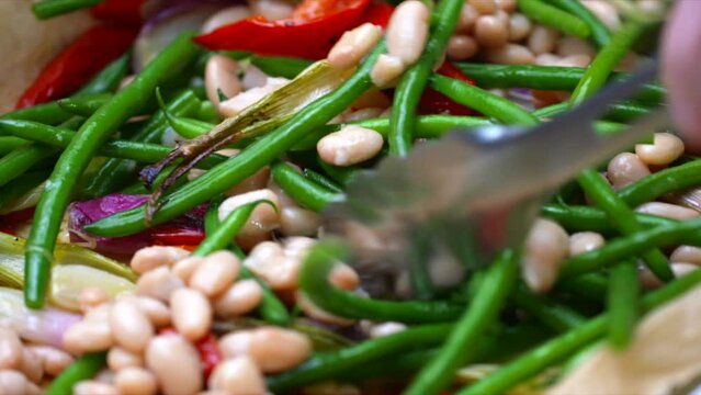 Beans in roasting tray. White and green beans with red peppers and scallions. Vegetables tossed with olive oil. Shallow depth of field footage of plant based cooking.