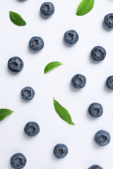 Tasty fresh blueberries with green leaves on white background, flat lay