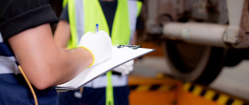 Closeup hands engineer man and woman or worker checking electric train for planning maintenance writing document on clipboard in station, transport and infrastructure, inspector check transport.