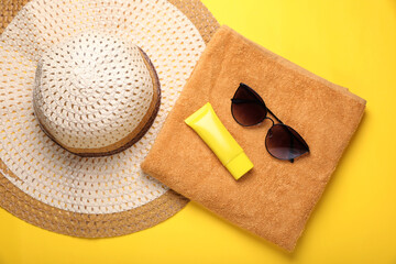 Straw hat, stylish sunglasses, towel and sunscreen on yellow background, flat lay. Beach accessories