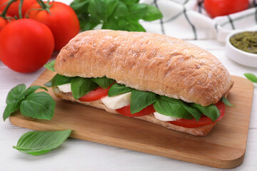 Delicious Caprese sandwich with mozzarella, tomatoes and basil on white wooden table, closeup