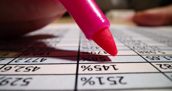 Pink marker on piece of paper with printed financial numerical data table and marked numbers