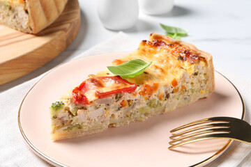 Piece of tasty quiche with chicken, cheese, basil and vegetables on white table, closeup