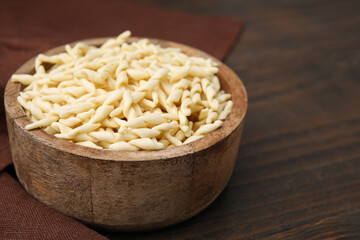 Uncooked trofie pasta in bowl on wooden table, closeup