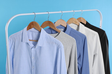 Rack with stylish clothes on wooden hangers against light blue background