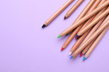 Many colorful pastel pencils on violet background, flat lay and space for text. Drawing supplies