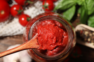 Taking tasty tomato sauce with wooden spoon from jar on table, top view