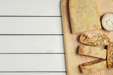 Tasty strudel with chicken, vegetables and sauce on white wooden table, top view. Space for text