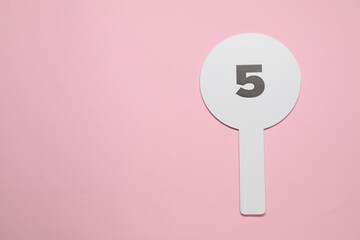 Auction paddle with number 5 on pink background, top view. Space for text
