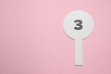 Auction paddle with number 3 on pink background, top view. Space for text