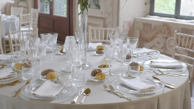 4k orbit around beautifully decorated wedding dinner table with classy cutlery, glasses, bread and flower arrangement. Bright, light flooded big room in old italian style manor lodge with paintings