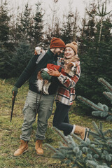 Couple with their dog having fun during Christmas tree harvesting at Eco Pine and Fir tree Farm. Casually dressed Happy family with Cavalier King Charles Spaniel hanging out outdoors, Holiday season.