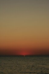 Naklejka na ściany i meble Beautiful red sunset over a serene ocean with tranquil waves crashing onto the shoreline