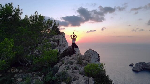 Dramatic aerial top view flight 
Ibiza cliff Yoga tree pose model girl sunset evening. panorama overview drone
4k cinematic