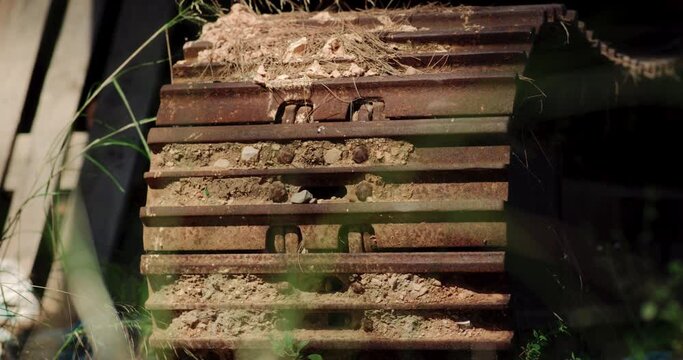 Shadows dance across heavy machinery track wheels caked with dried mud and grass