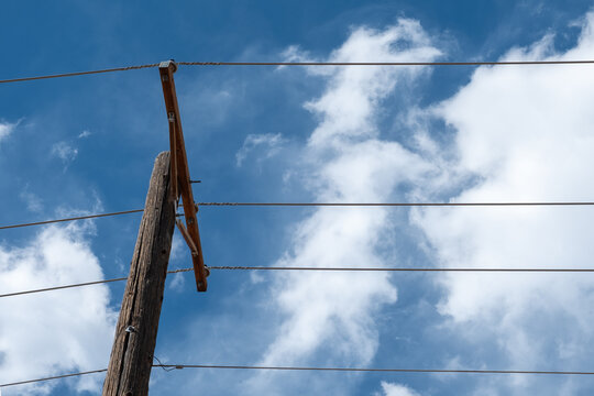 Looking Up At A Wooden Telephone Pole And Power Lines With Blue Sky And White Clouds Overhead.