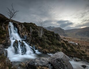 Fototapeta premium Majestic waterfall cascades down a rugged hillside in the Y Garn Mountains of Wales