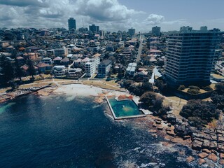 Aerial view of a tropical beach with rows of colorful beach houses in Fairlight Rock Pool, Sydney