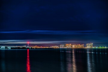 a nighttime sky over the ocean with city lights on and a boat out to sea