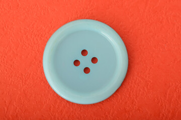 Blue sewing button isolated on a red background.