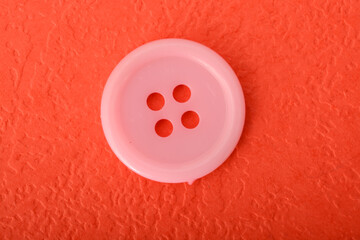 Pink sewing button isolated on a red background.