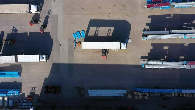 Trucks with semi-trailers stand on the parking lot of the logistics park with loading hub and wait for load and unload goods at warehouse ramps at sunset. Aerial view